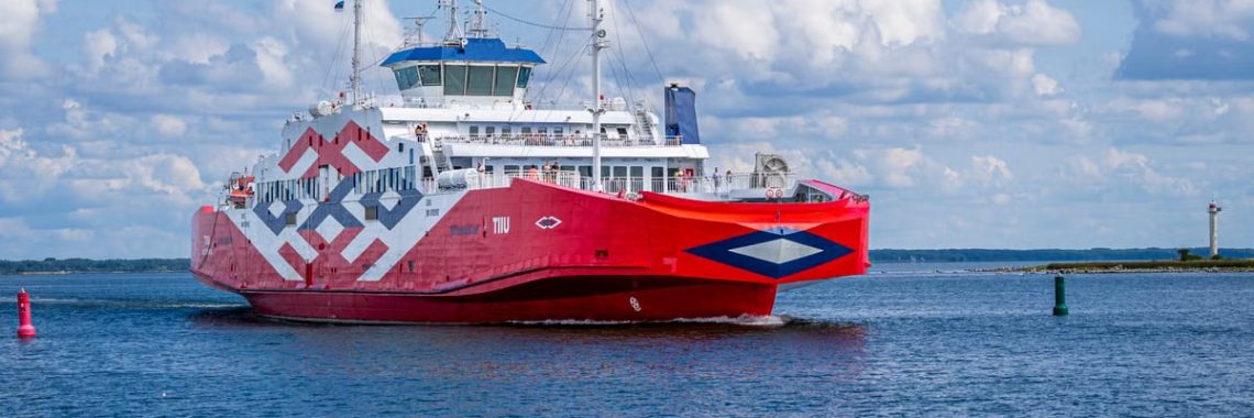 A striking red ferry sails through serene waters in Hiidenmaa, Finland, under a clear blue sky.