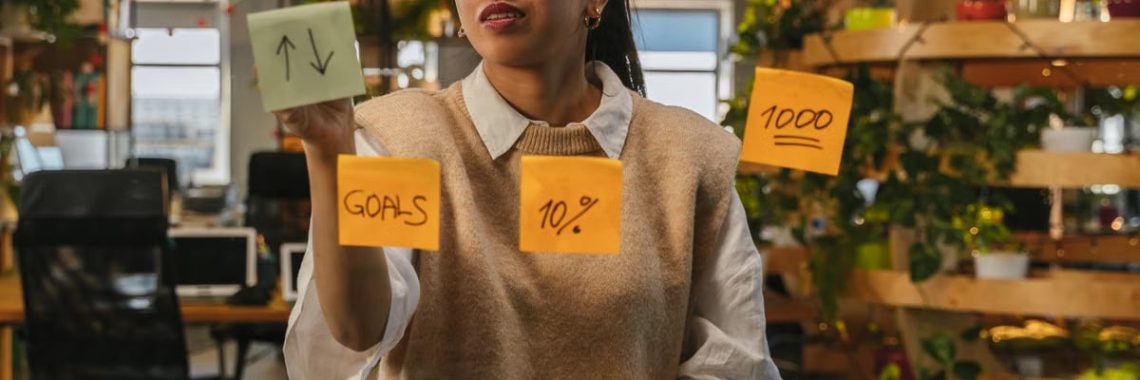 Asian woman organizing tasks on sticky notes at modern office workspace.